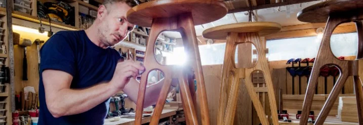 Person trägt Lack auf Holzhocker auf