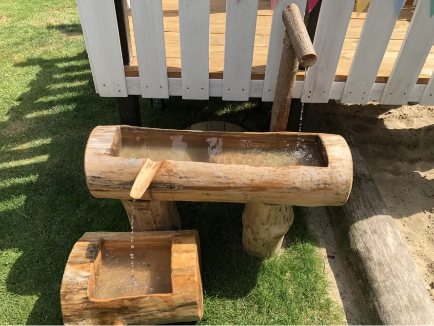 Wasser rinnt aus einem Holzrohr in ein Holzbecken
