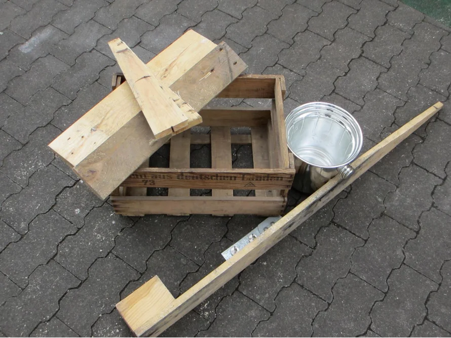 Holzkiste, Bretter und ein Metalleimer auf Pflastersteinen