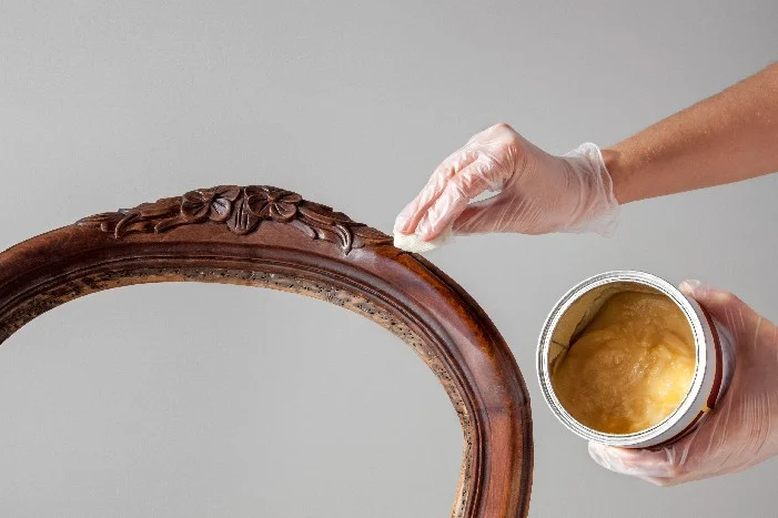 Person trägt Wachs auf antiken Stuhlrahmen auf