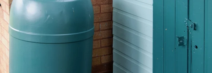 Eine grüne Regentonne steht an einer Hauswand.