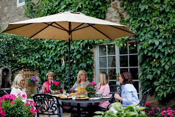 Eine Gruppe von Personen sitzt unter einem Sonnenschirm an einem Gartentisch.