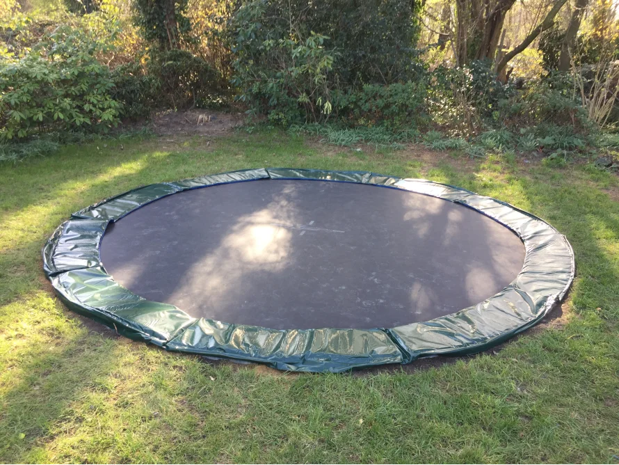 Ein Trampolin mit grüner Abdeckung auf einem Rasen.