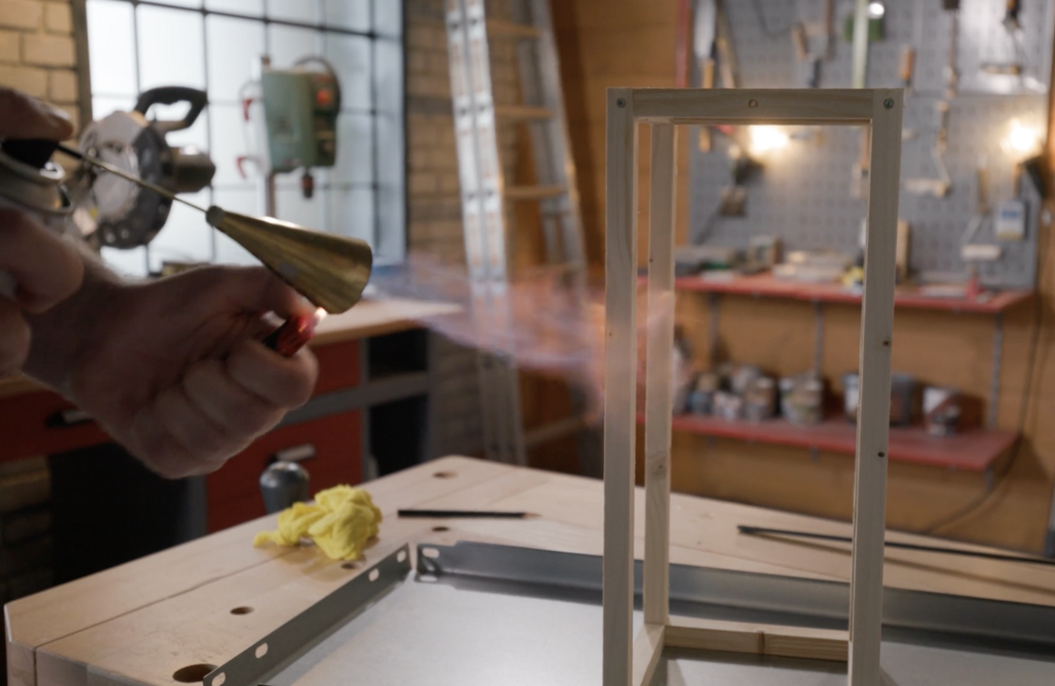 Person bearbeitet Holzrahmen mit Gasbrenner