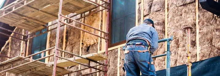 Person bringt Dämmmaterial an Hauswand an