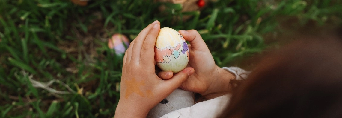 Ein Kind hält ein bemaltes Osterei in den Händen.