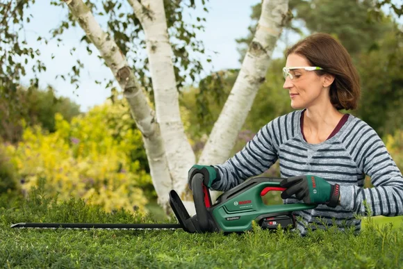 Person mit Schutzbrille und Heckenschere