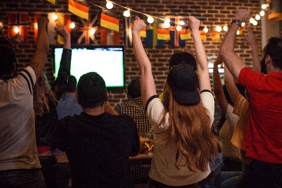 Menschen schauen ein Fußballspiel und feiern mit erhobenen Armen.