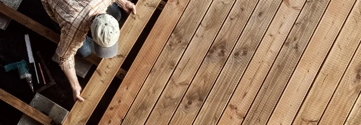 Person verlegt Holzdielen auf einer Terrasse.