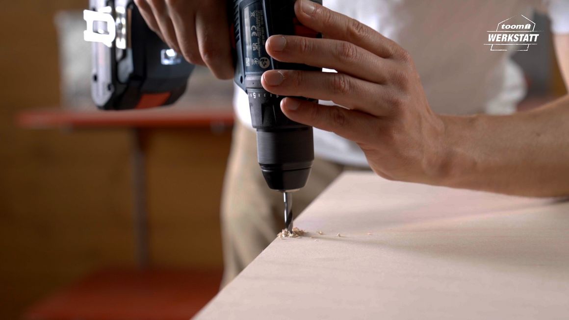 Person bohrt mit einem Akkuschrauber in eine Holzplatte