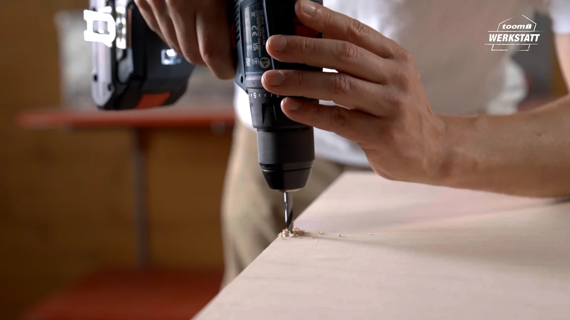 Person bohrt mit einem Akkuschrauber in eine Holzplatte