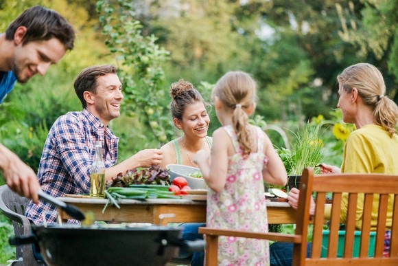 Eine Person grillt mit einer Grillzange für eine Gruppe von Menschen im Garten.