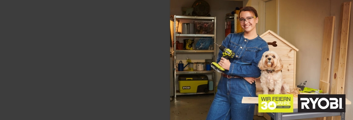 Lächelnder Mensch mit Hund und Akkuschrauber in einer Werkstatt.