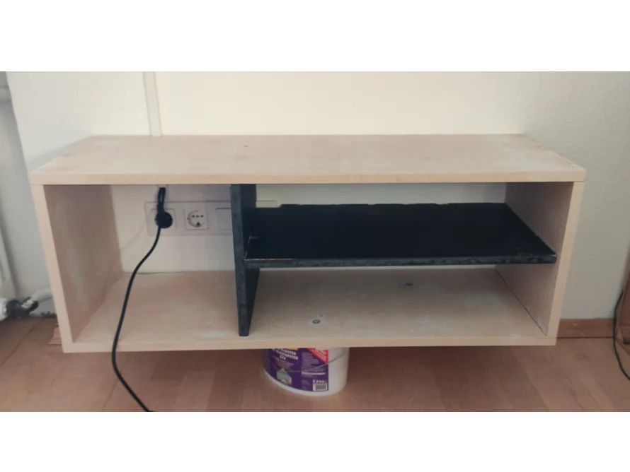 Ein Wandregal aus hellem Holz mit einem schwarzen Einlegeboden.