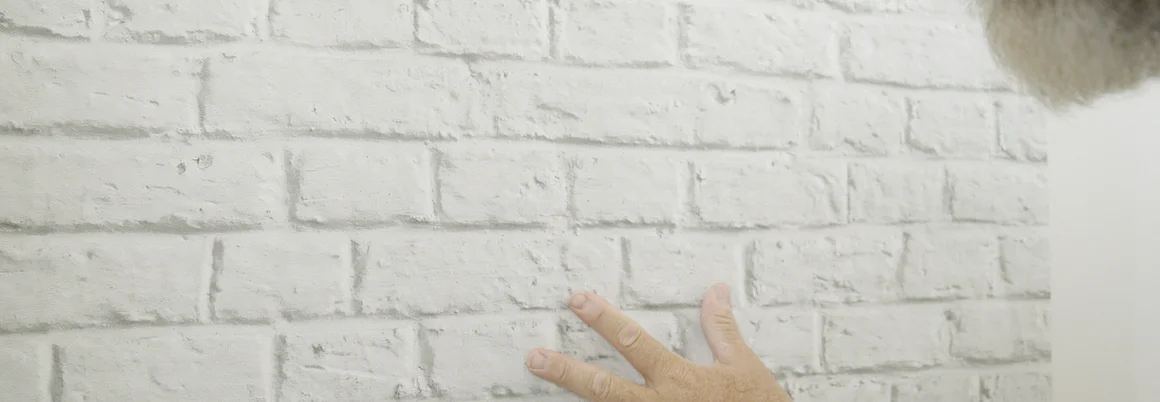 Person berührt weiße Ziegelwand