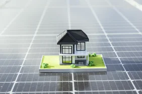 Ein kleines Hausmodell steht auf einem Solarpanel.