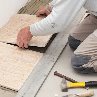 Person verlegt Fliesen mit Gummihammer