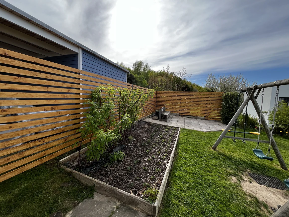 Ein Garten mit einem Zaun aus Holzlatten und einer Schaukel.