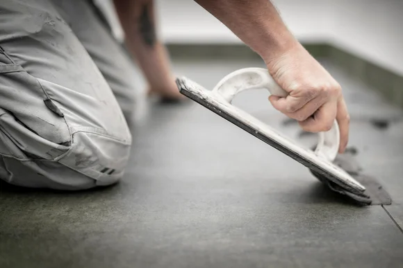 Person verlegt Fliesen mit Kelle.