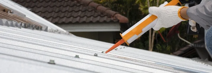 Person verwendet Dichtmittel auf einem Metalldach.
