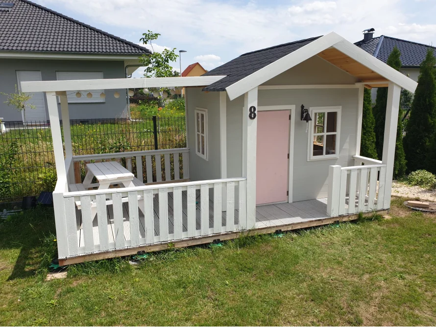 Graues Spielhaus mit Veranda und rosa Tür.