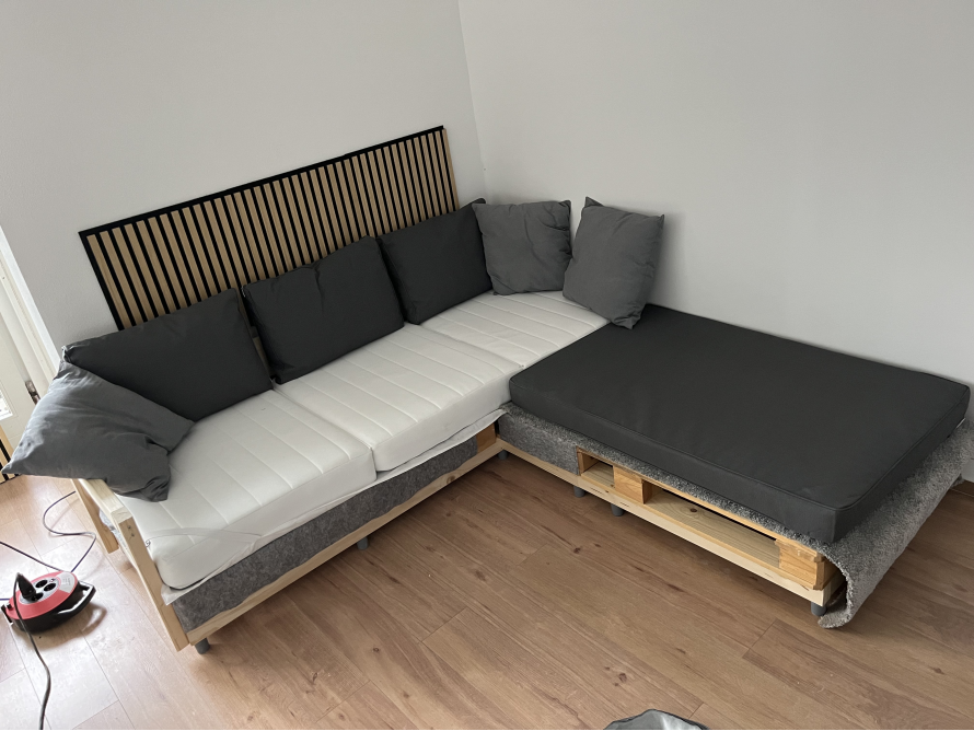 Selbstgebautes Ecksofa aus Holz mit weißen Matratzen und grauen Kissen