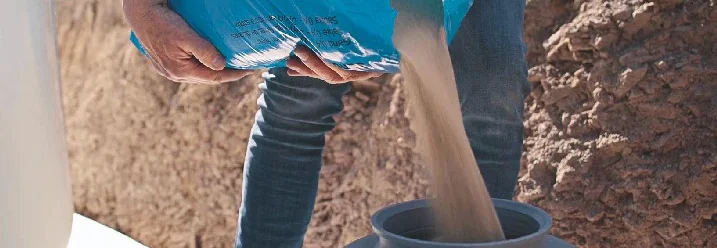 Person füllt Sand aus einem Sack in einen Filter