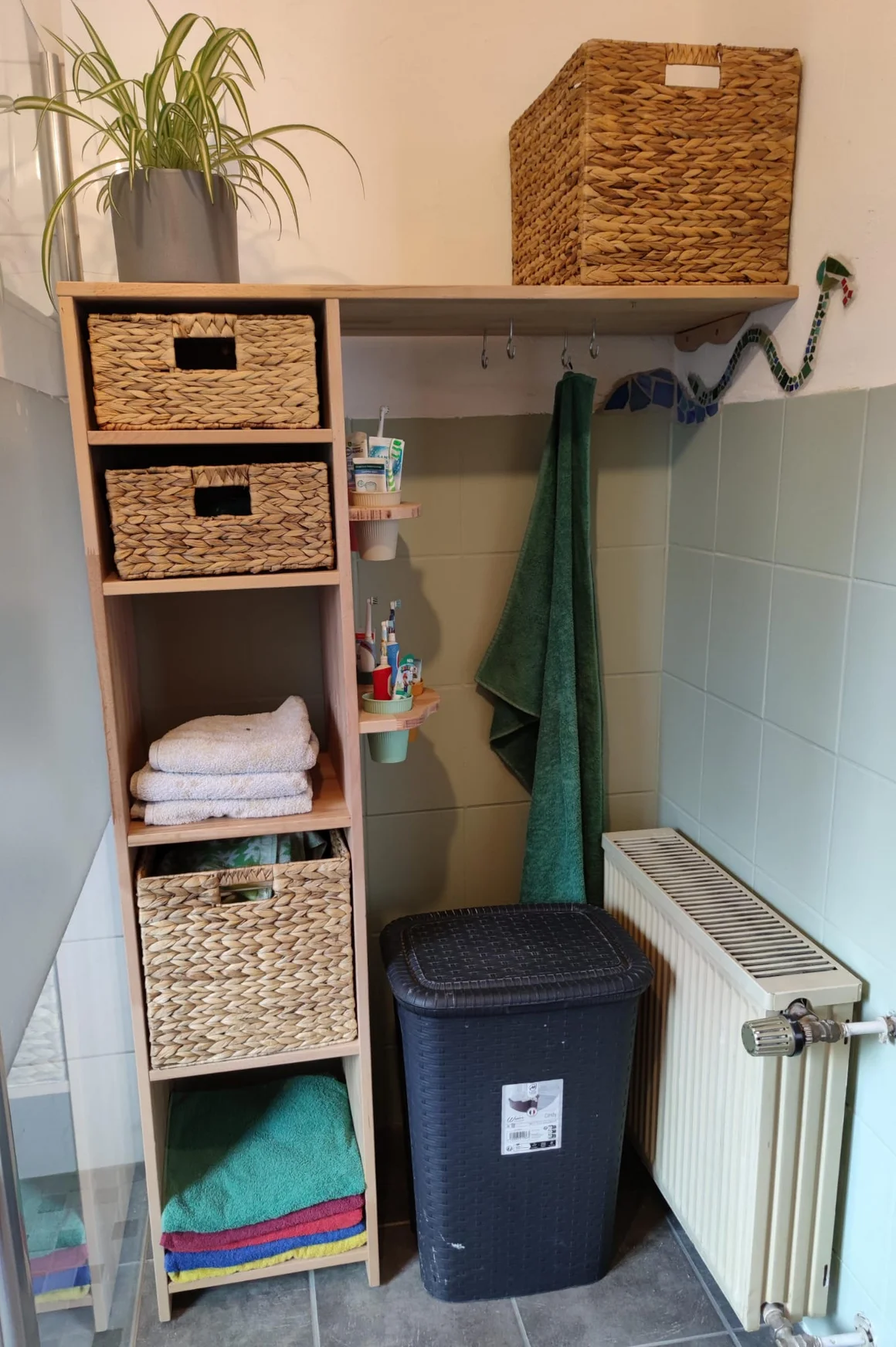 Badezimmerecke mit einem schmalen Holzregal, Körben, Handtüchern und einem Wäschekorb.