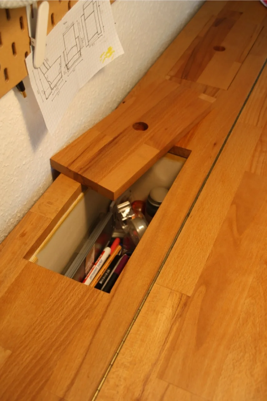 Geöffnetes Staufach in einer Schreibtischplatte aus Holz, gefüllt mit Stiften.
