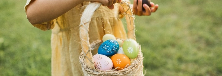 Ein Kind hält einen Korb mit bunten Ostereiern in der Hand.