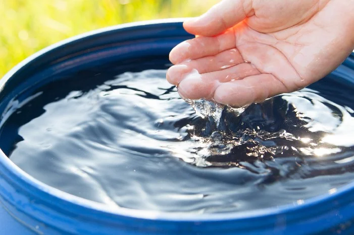 Hand fängt Wasser aus Regentonne auf