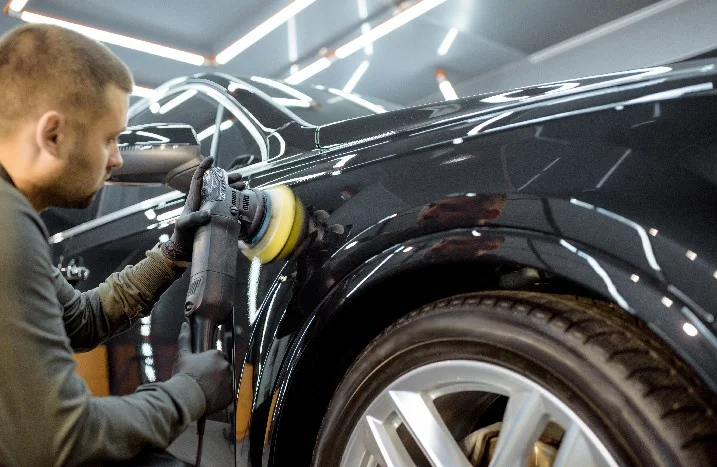 Person poliert ein schwarzes Auto mit einer Poliermaschine.
