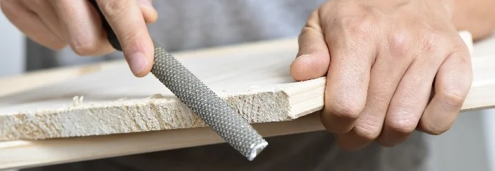 Person feilt Holzbrett mit Feile