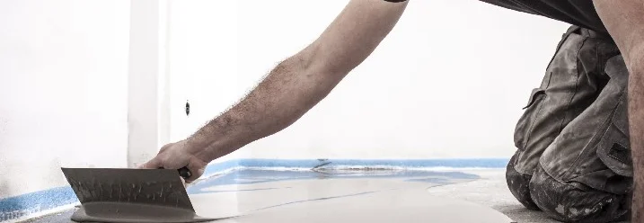 Person verteilt Spachtelmasse auf einem Boden