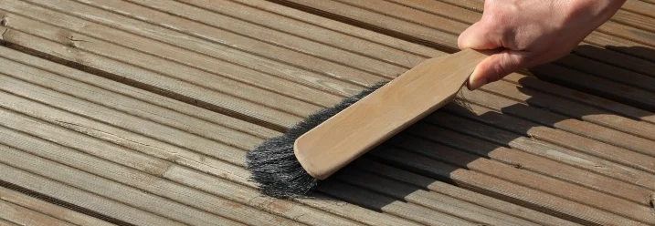 Hand fegt Holzterrasse mit Bürste
