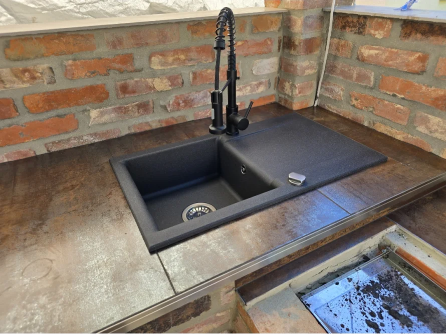 Schwarzes Spülbecken mit Wasserhahn in rustikaler Außenküche.