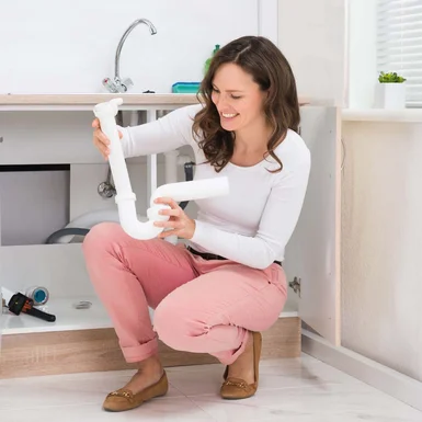 Person tauscht Siphon unter Spüle