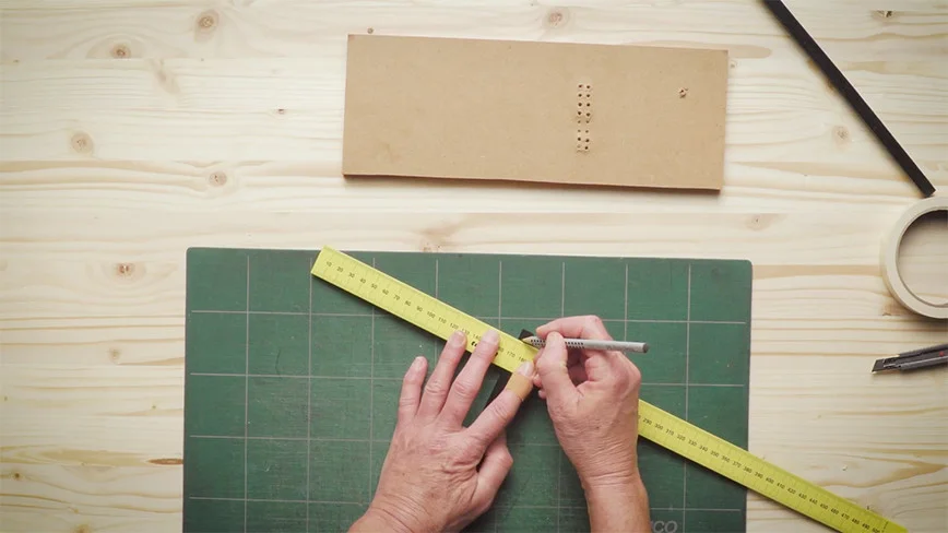 Zwei Hände zeichnen mit einem Bleistift eine Linie auf ein Stück Holz.