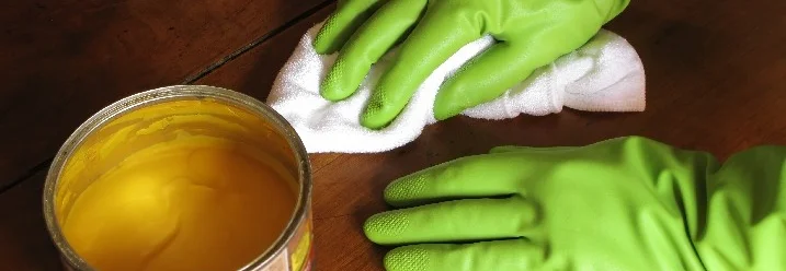 Person trägt gelbe Politur mit Tuch auf Holztisch auf