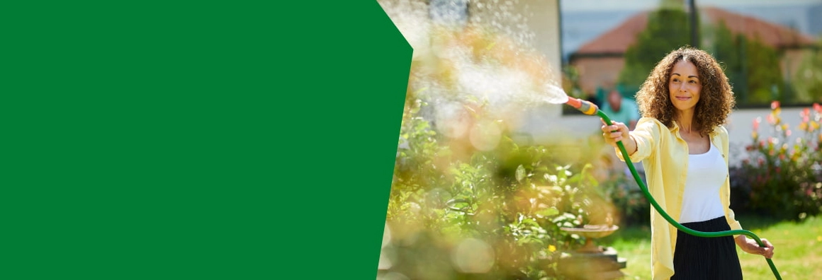 Person bewässert Pflanzen im Garten mit einem Schlauch.