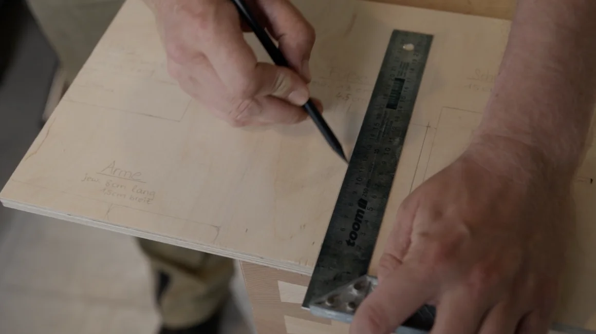 Hände zeichnen mit einem Bleistift und einem Winkel Lineal auf einer Holzplatte Linien ein.