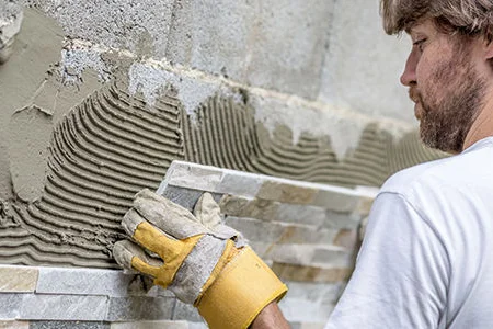 Person bringt Fliesen an Wand an