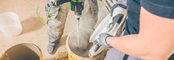 Zwei Personen mischen mit einem Rührgerät Beton in einem Eimer.