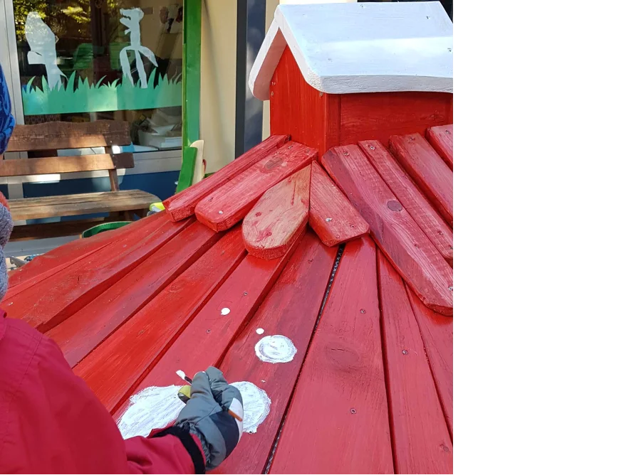 Person streicht rotes Holzdach weiß an