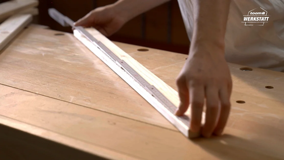 Person misst Holzbrett mit Zollstock ab