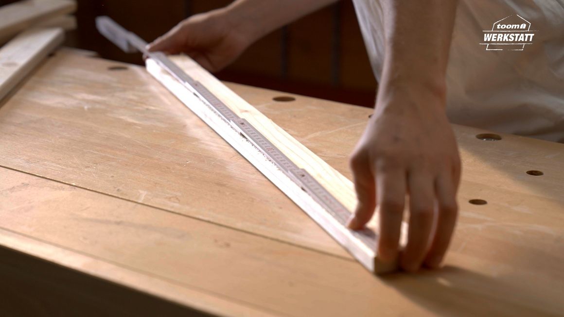 Person misst Holzbrett mit Zollstock ab