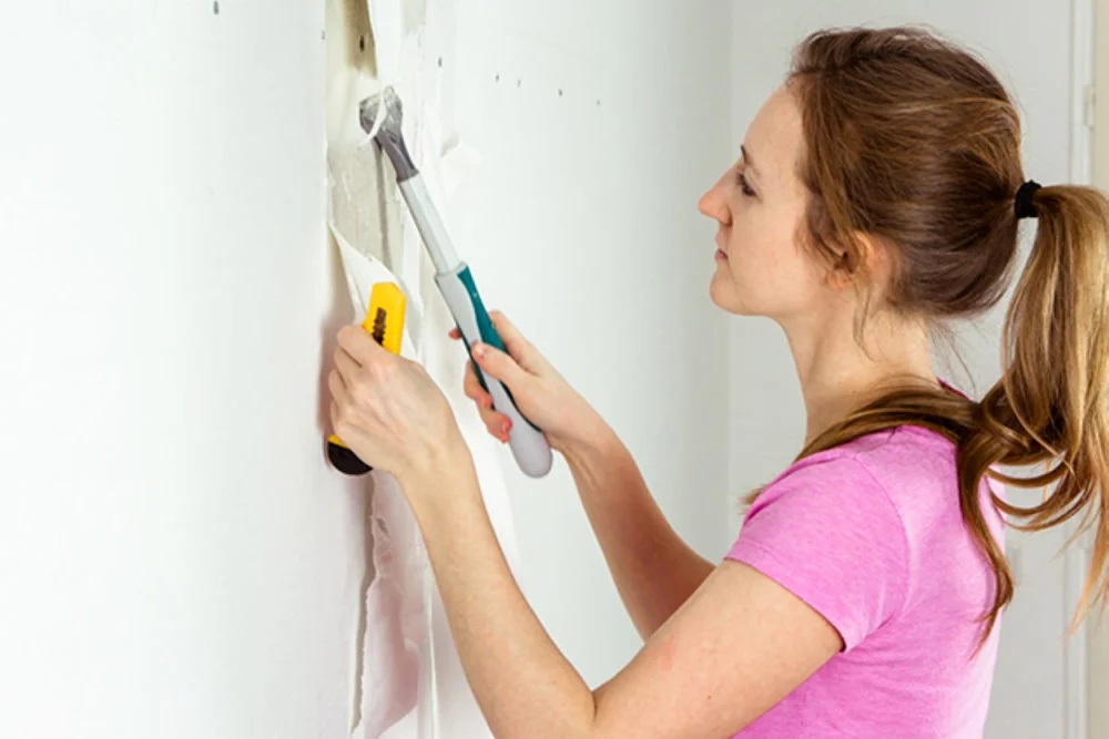 Person entfernt Tapete mit Spachtel