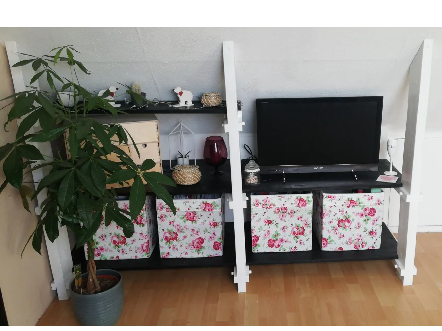 Ein weißes Regal mit einem Fernseher und Aufbewahrungsboxen.