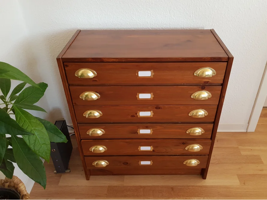 Eine Kommode aus dunklem Holz mit sechs Schubladen und goldenen Griffen.