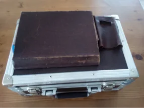 Ein alter, brauner Lederkoffer mit einem Buch und einer Ledertasche darauf.